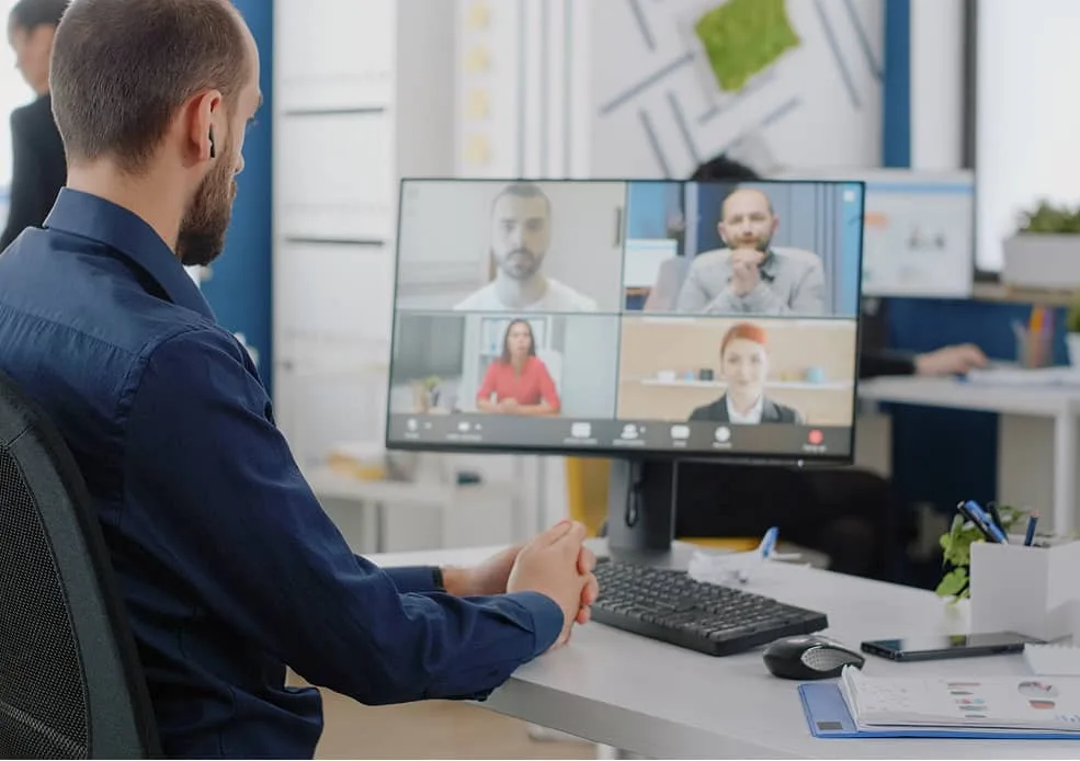Mann nimmt an Videomeeting mit vier Teilnehmern am Monitor teil