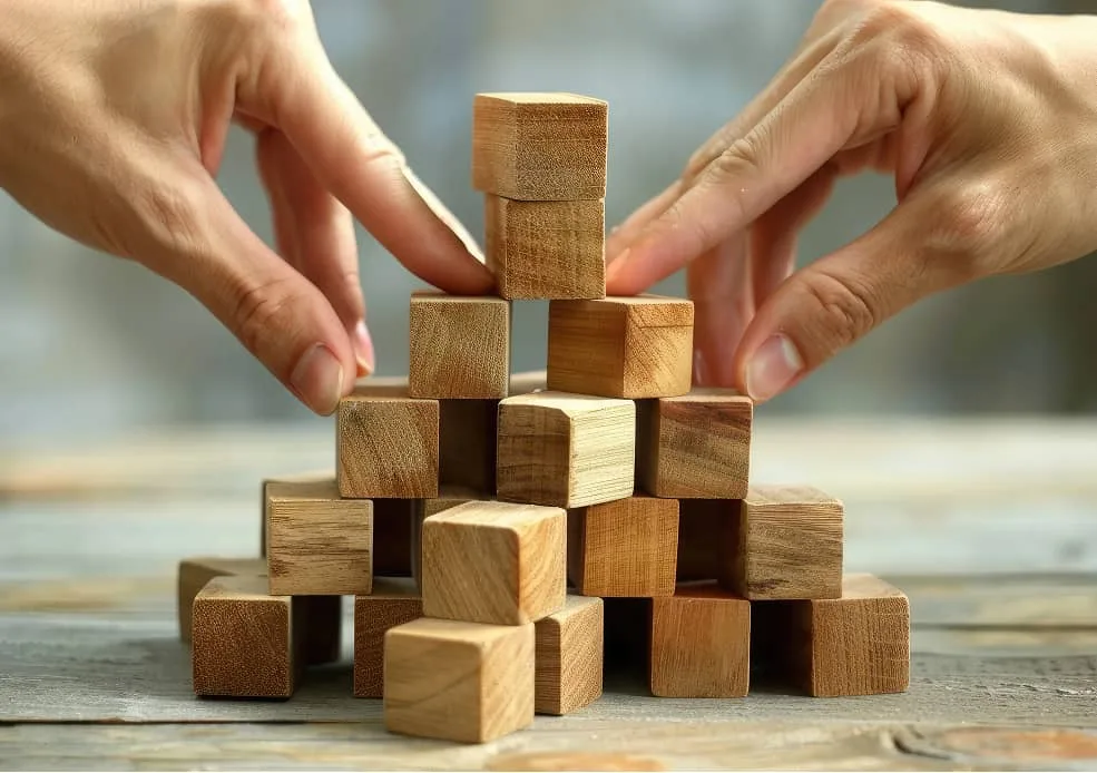 Zwei Hände stapeln gemeinsam Holzwürfel zu einer Pyramide