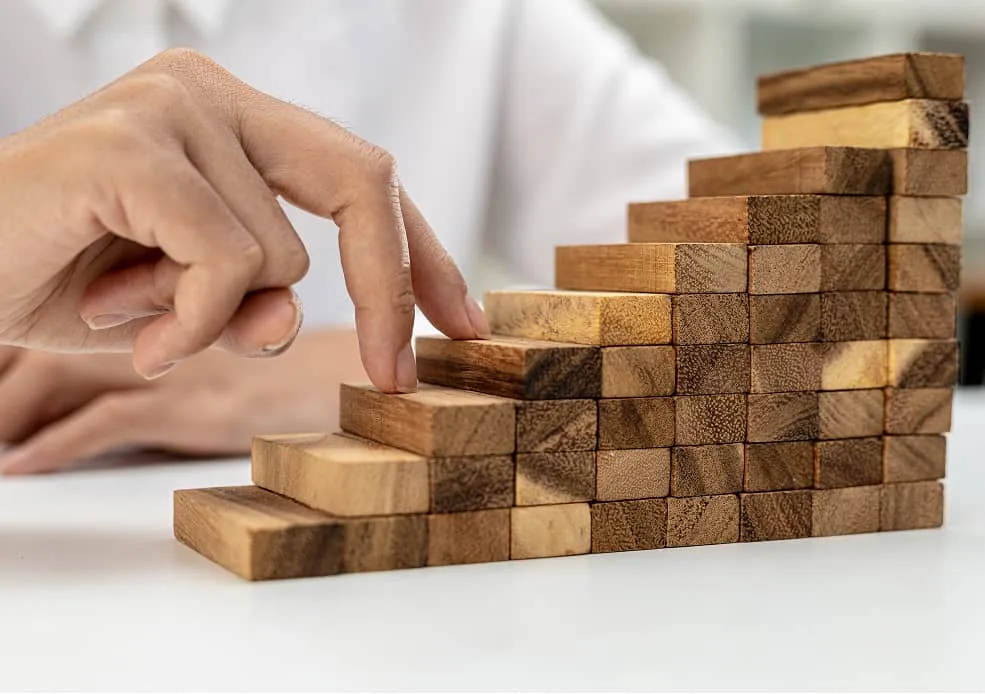 Hand stapelt Holzklötze als Treppe – Symbol für Auftraggeber-Perspektive