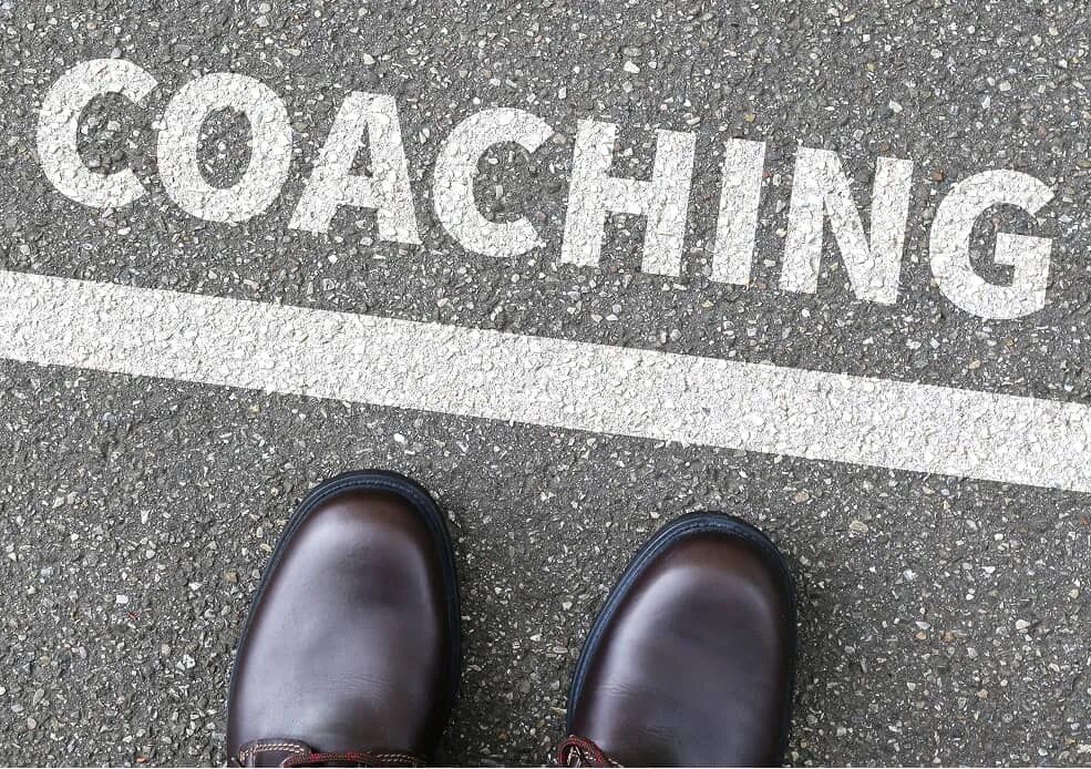 Schuhe stehen vor dem Schriftzug Coaching auf Asphalt