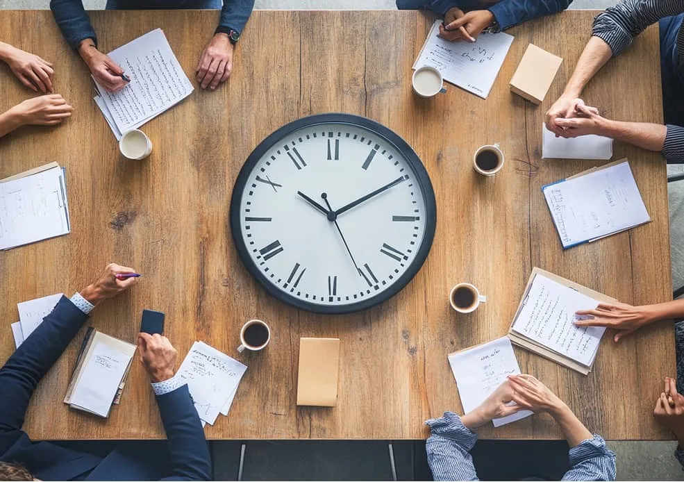 Team arbeitet an rundem Tisch mit Uhr in der Mitte